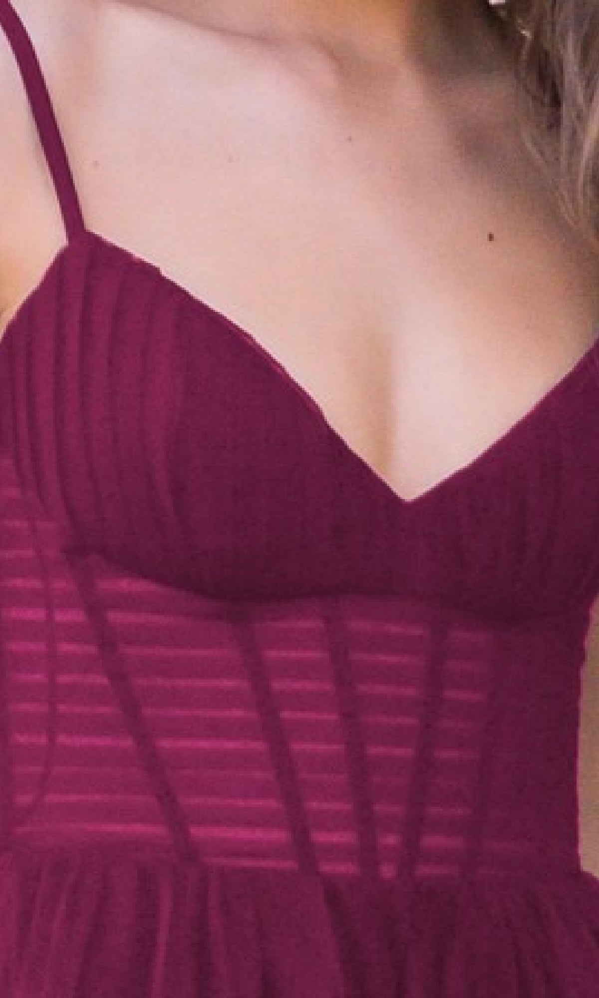 A close-up of a person wearing the Yasmin by Velvi Sheer-Corset Long Prom Ball Gown in burgundy, featuring a sleeveless design and sheer striped panels on the bodice.